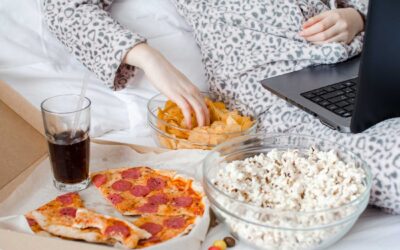 Person with laptop in lap eating pepperoni pizza, popcorn, chips and soda